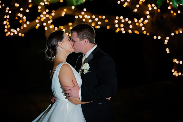 Newly married couple kissing with fairy lights in the background